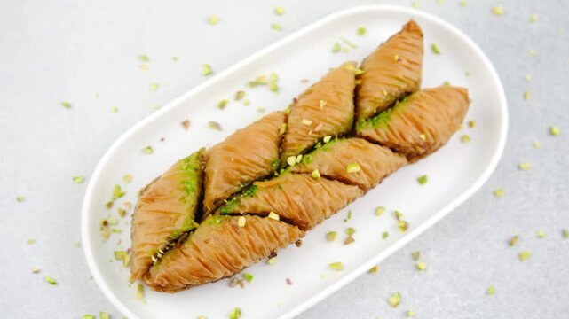 Pieces of baklava dessert sprinkled with crushed pistachios on a white oval plate