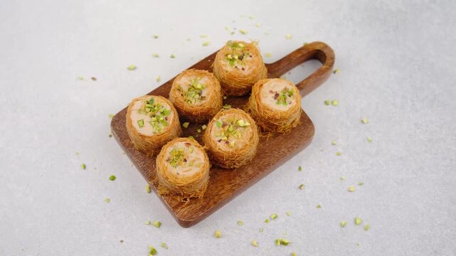 Sweet rolled baklava pastries with chopped pistachios on a wooden board