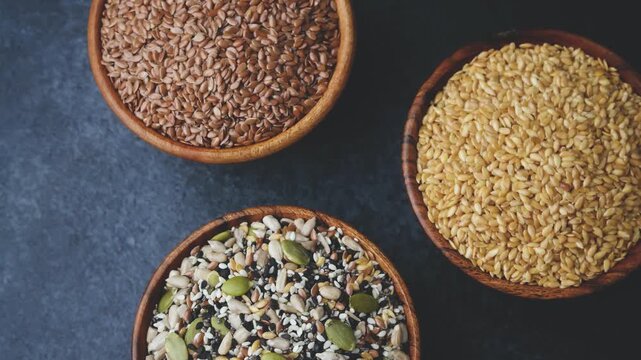Three wooden bowls filled with mixed seeds and grains on a dark background