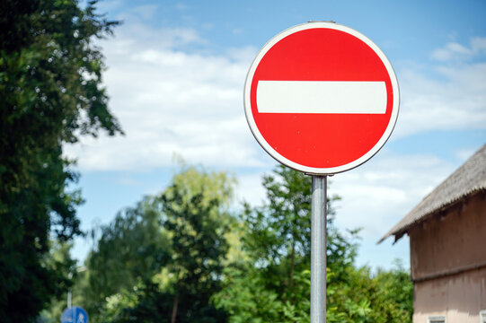 Red no entry sign stands in front of trees and a building on a clear day