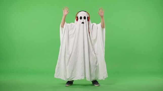 Person in ghost costume wearing headphones dancing against a green screen background