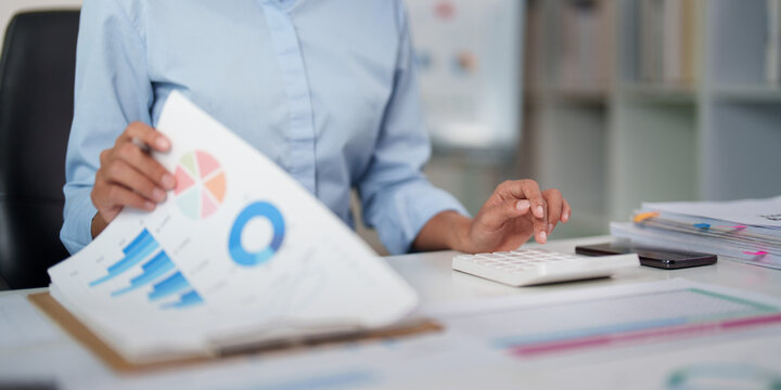 Businesswoman using calculator and analyzing financial report charts at office desk