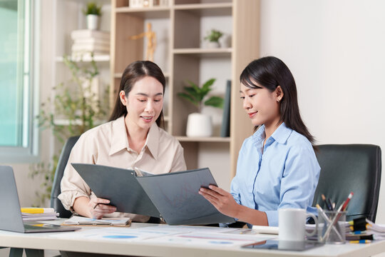 Asian businesswomen discussing document folder and digital technology strategy at office desk