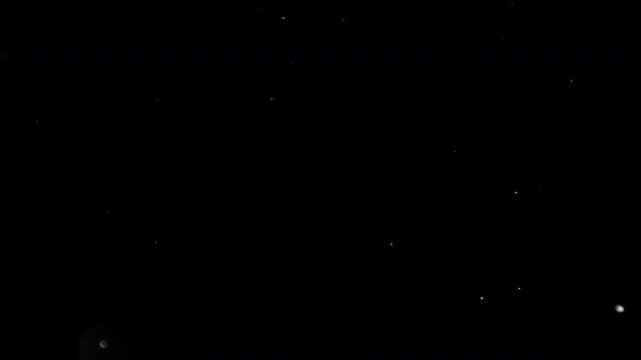 Super slow motion video at 1000 fps showing tiny particles floating and moving through the air against a black background, revealing intricate motion and atmospheric detail.