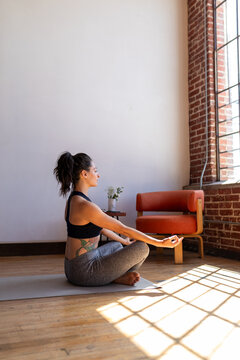 Person meditating in a sunlit room with brick walls and wooden floor.