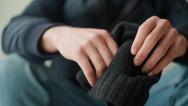 Close up of hands inspecting pair of black knit gloves with visible texture and small debris. person examines material closely focusing on details like ribbed pattern or wear. Soft lighting