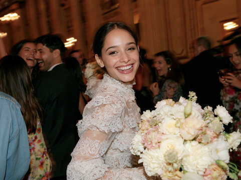 Portrait of radiant bride smiling happily holding lush white bouquet surrounded by guests at reception