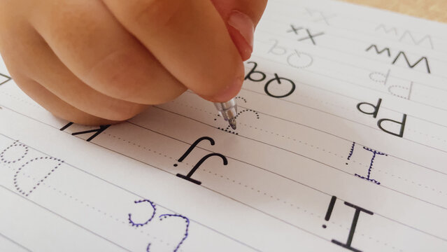 Macro close up view of child hand holding pen tracing dotted English alphabet letters J and I in handwriting practice notebook horizontal stock photo