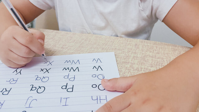 Medium close up top view of child sitting at table writing English letters with pen in alphabet practice workbook page horizontal stock photo