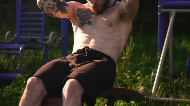 Man doing sit-ups in an outdoor fitness area surrounded by green grass in the morning sun