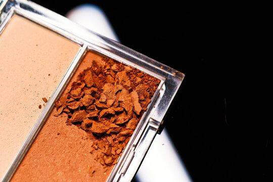Makeup palette shows broken bronzer and pressed powder on a dark surface