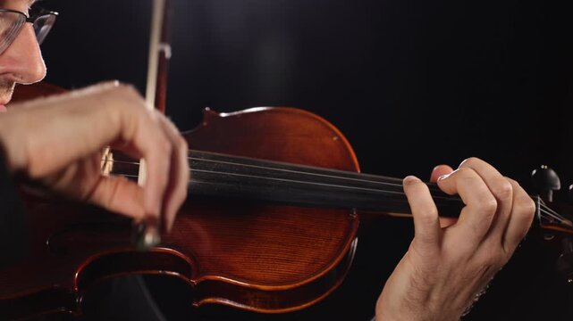 Close-up video of a violinist playing, focusing on hands, bow, and vibrating strings against a black background, capturing musical performance, movement, rhythm, and detail.
