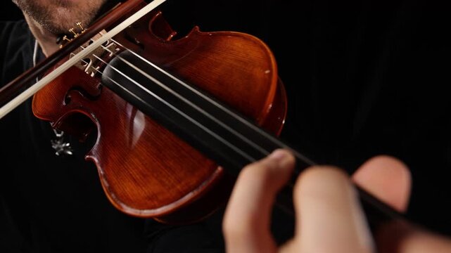 Close-up video of a violinist playing, focusing on hands, bow, and vibrating strings against a black background, capturing musical performance, movement, rhythm, and detail.