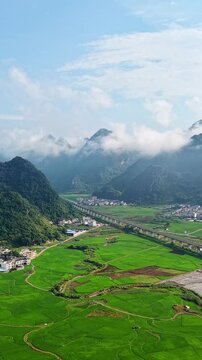 Vertical Video: High-speed train gliding through the clouds above rural karst hills with mist filling the valleys
