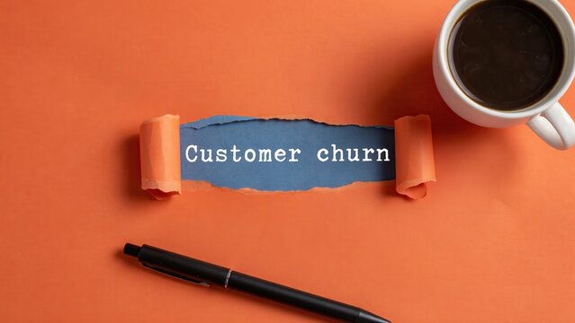 Customer churn text revealed through torn orange paper with coffee and pen on desk. Business marketing concept for client retention strategy.