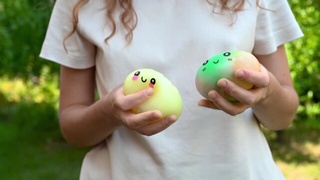 Girl holding and squeezing colorful dumpling-shaped squishy toys with cute faces outdoors. Sensory play, tactile activity, relaxation and stress relief concept.