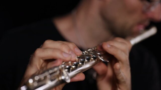 Close-up video of a flutist playing a transverse flute, focusing on hands, fingers, keys, and instrument details against a black background, capturing technique and musical movement.