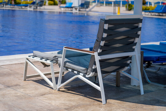 Comfortable modern outdoor lounge chair with ottoman situated on sunny poolside patio at luxury resort, perfect for relaxation and summer vacation leisure in sun.