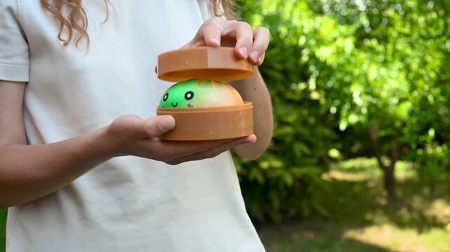 Girl playing with a dumpling shaped squishy toy out of a box and pressing in her hands outdoors. Sensory fidget, tactile stimulation, relaxation and playful activity concept.