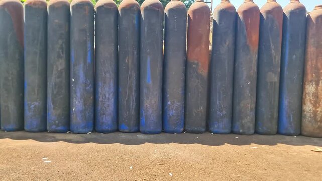 Row of Weathered Industrial High Pressure Gas Cylinders Standing Outdoors