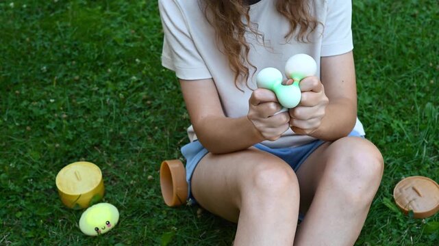 Girl sitting on the grass and playing with colorful dumpling-shaped squishy toys. She holds and manipulates the soft toys in her hands during a relaxing sensory activity.