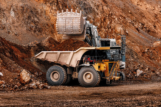 Big mining dump truck being loaded golden ore by excavator in open pit quarry for industrial and heavy equipment background