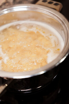 Pasta boiling in bubbling water on stove in stainless steel pot. 