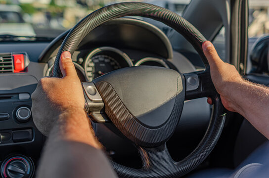 A person holds the steering wheel while driving a car during daylight hours.