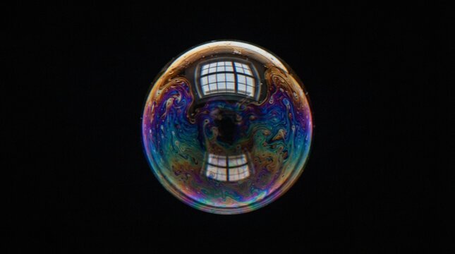 A soap bubble with vibrant iridescent colors and reflections of a window pane isolated against a deep black background.