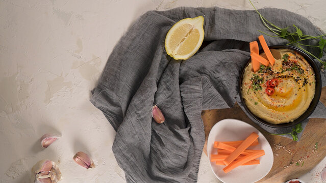 Hummus bowl with carrot sticks and lemon on a board