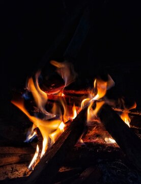 Glowing orange campfire flames and burning wood logs in the dark