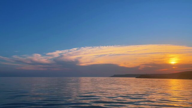Scenic panning shot of a golden sunset over a calm blue sea with glowing clouds and water reflections in Saros Gulf, Edirne, Turkey.