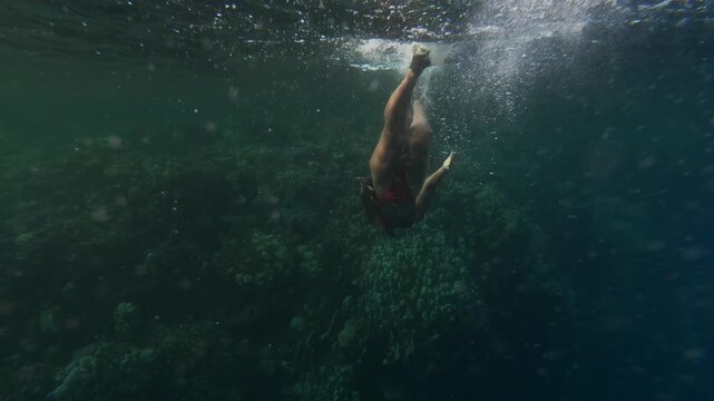 Woman descending underwater with fins on breath hold dive, recreational freediving and snorkeling in tropical sea