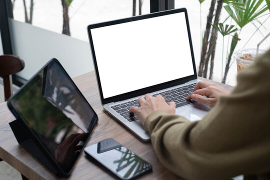 Asian professional typing on a laptop at a cafe table with tablet and smartphone, featuring a blank screen for copy space. Modern digital workspace concept for business, technology, and productivity.