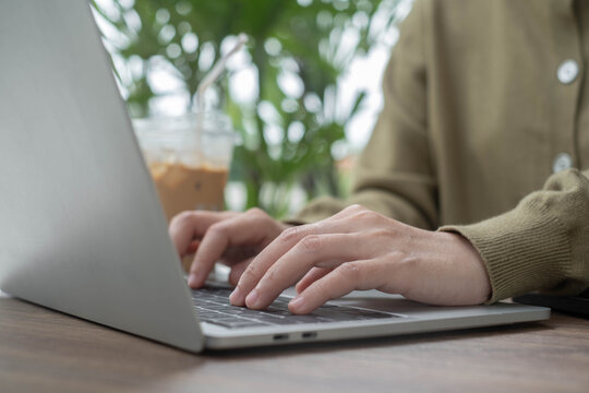 Person typing on a laptop at a cozy cafe table with iced coffee, representing remote work, digital productivity, online business, technology, flexible work, and a modern professional lifestyle.