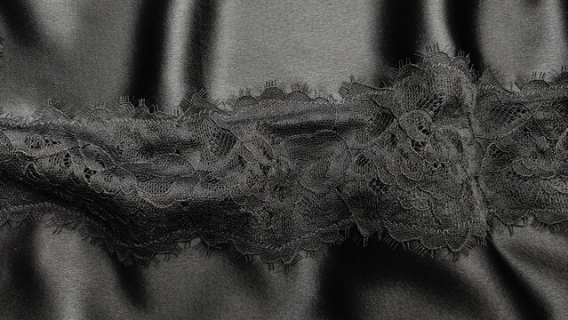 Close-up of elegant black lace and sheer fabric with intricate floral details and delicate texture, creating a dramatic dark textile background.