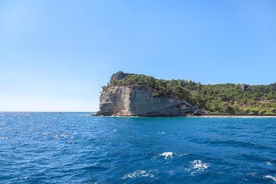 Picturesque view from a ship at sea, coastal white rocky cliffs with green trees the tops under a bright sunny sky during a summer voyage.