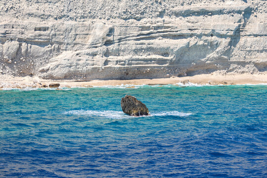 Picturesque view from a ship at sea, coastal white rocky cliffs with green trees on tops under a bright sunny sky during a summer voyage.