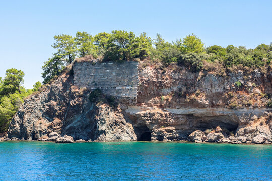 Picturesque view from ship sea, coastal white rocky cliffs with green trees tops under bright sunny sky during summer voyage.