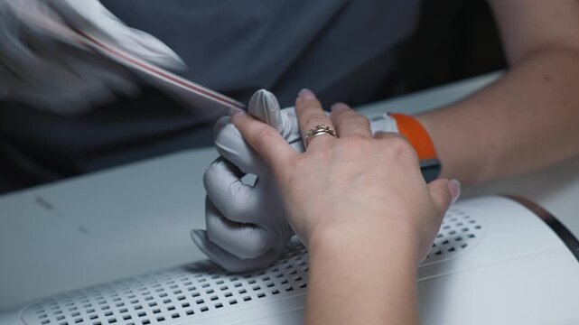 Acrylic nail shaping with file by manicure technician in beauty salon as part of professional nail modeling