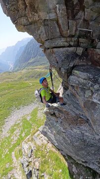 Male climber taking a break suspended on steep cliff wall, Via Ferrata Detomasi in Cimalegna near Monte Rosa.