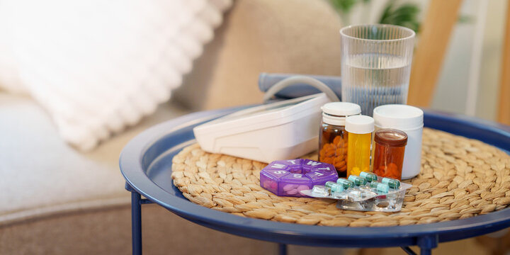 Medical pill bottles with daily organizer and digital blood pressure monitor on table at home