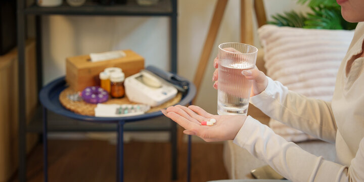 Woman holding pills and glass of water for daily healthcare routine at home