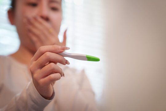 Woman holding pregnancy test stick in hand with shocked background expression