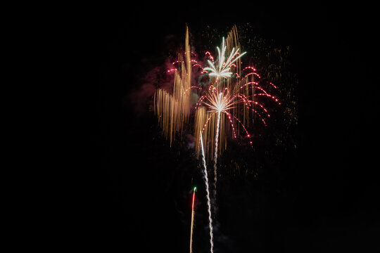Brilliant fireworks bursting with golden light trails against dark night sky during summer festival celebration