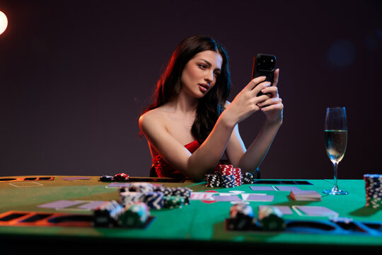 Online poker woman with a smartphone at a casino table with cards and chips.