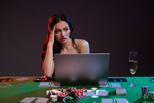 Sexy woman win lose emotion in red dress playing poker online in front of laptop and poker chips, holding cards