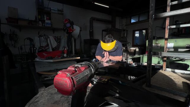 Focused artisan with a protective visor using a power drill on a stainless steel plate in a dim factory. Industrial craftsmanship and precision manufacturing