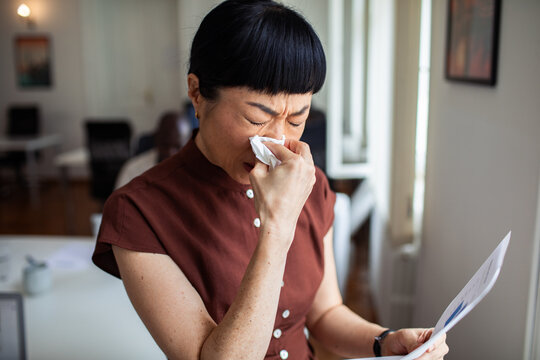 Woman with cold blowing nose at office