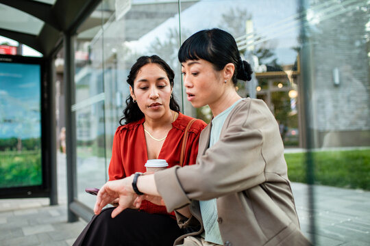 Two women checking time at urban bus stop